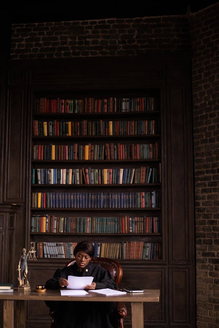 Black female judge reading papers at desk in office with bookshelves.